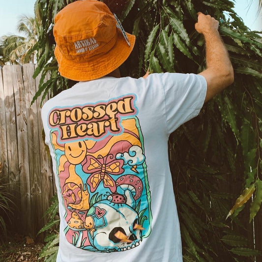 Person wearing white alternative streetwear t-shirt with colorful skull and butterfly back graphic by Crossed Heart Clothing outdoors