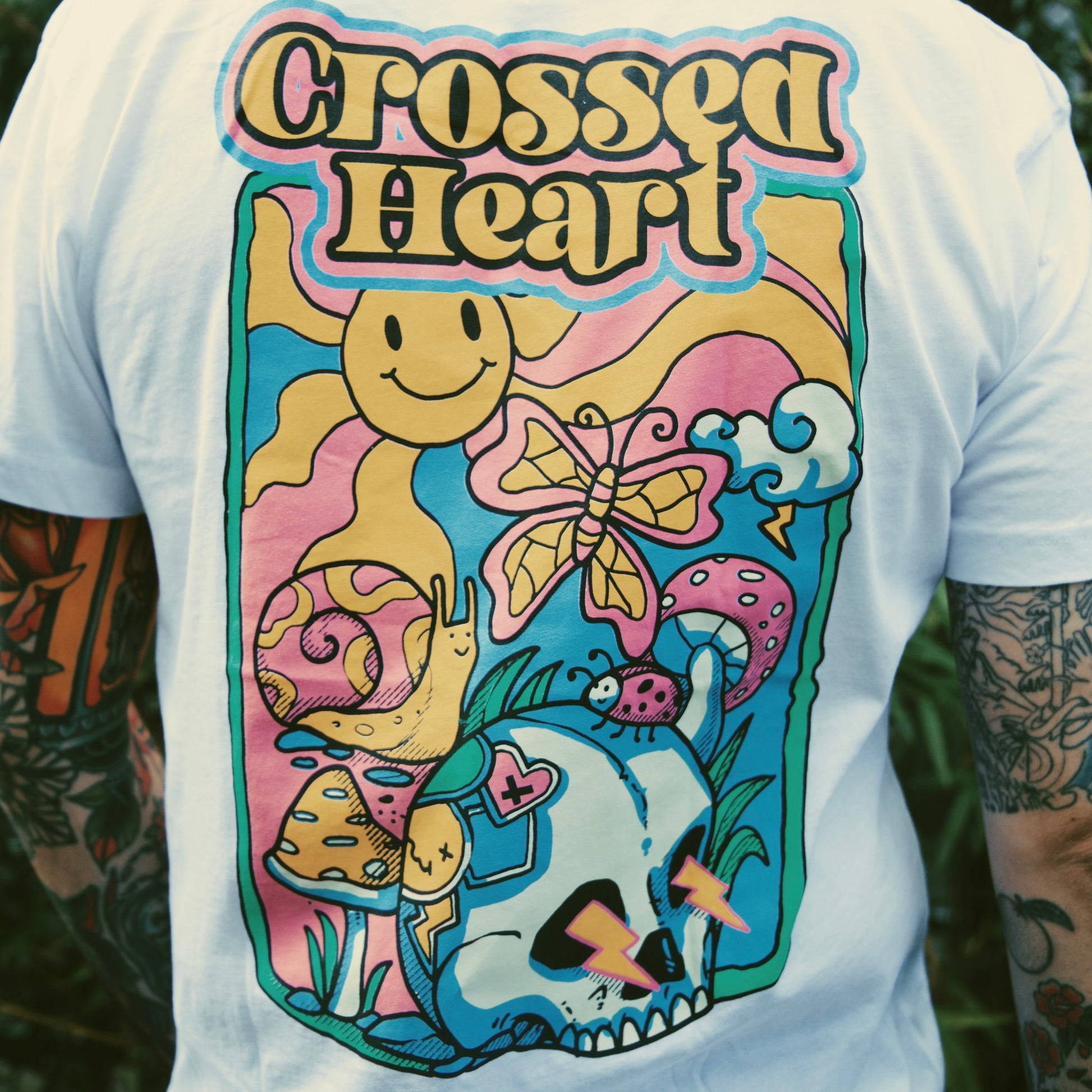 Close-up of colorful skull, butterfly, mushroom, and smiley graphic on white alternative streetwear t-shirt by Crossed Heart Clothing