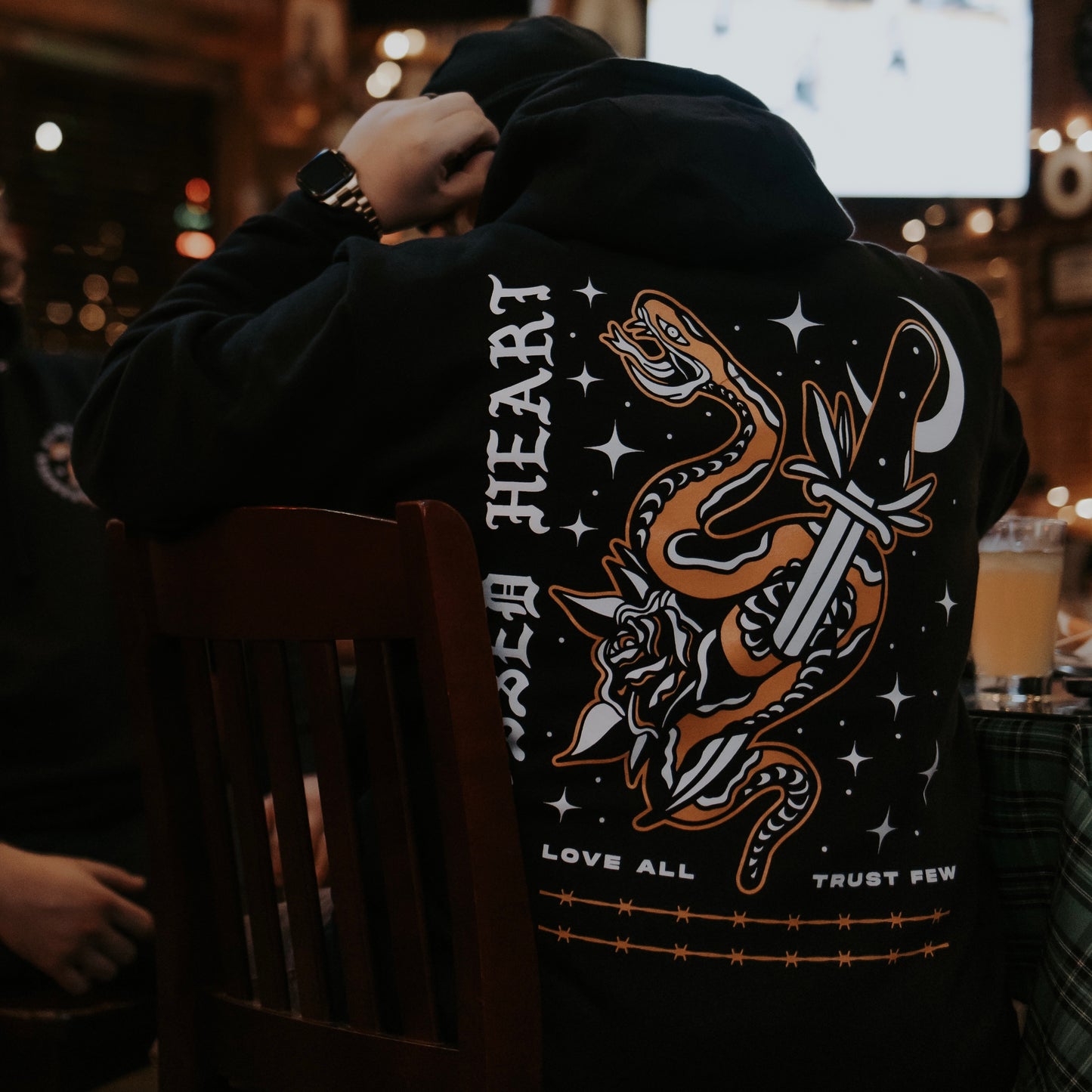 person wearing black love all trust few hoodie with snake and dagger graphic back print streetwear lifestyle photo
