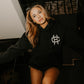 woman wearing true to the crew crossed heart black hoodie with chest logo tattoo inspired alternative streetwear hoodie indoor lifestyle