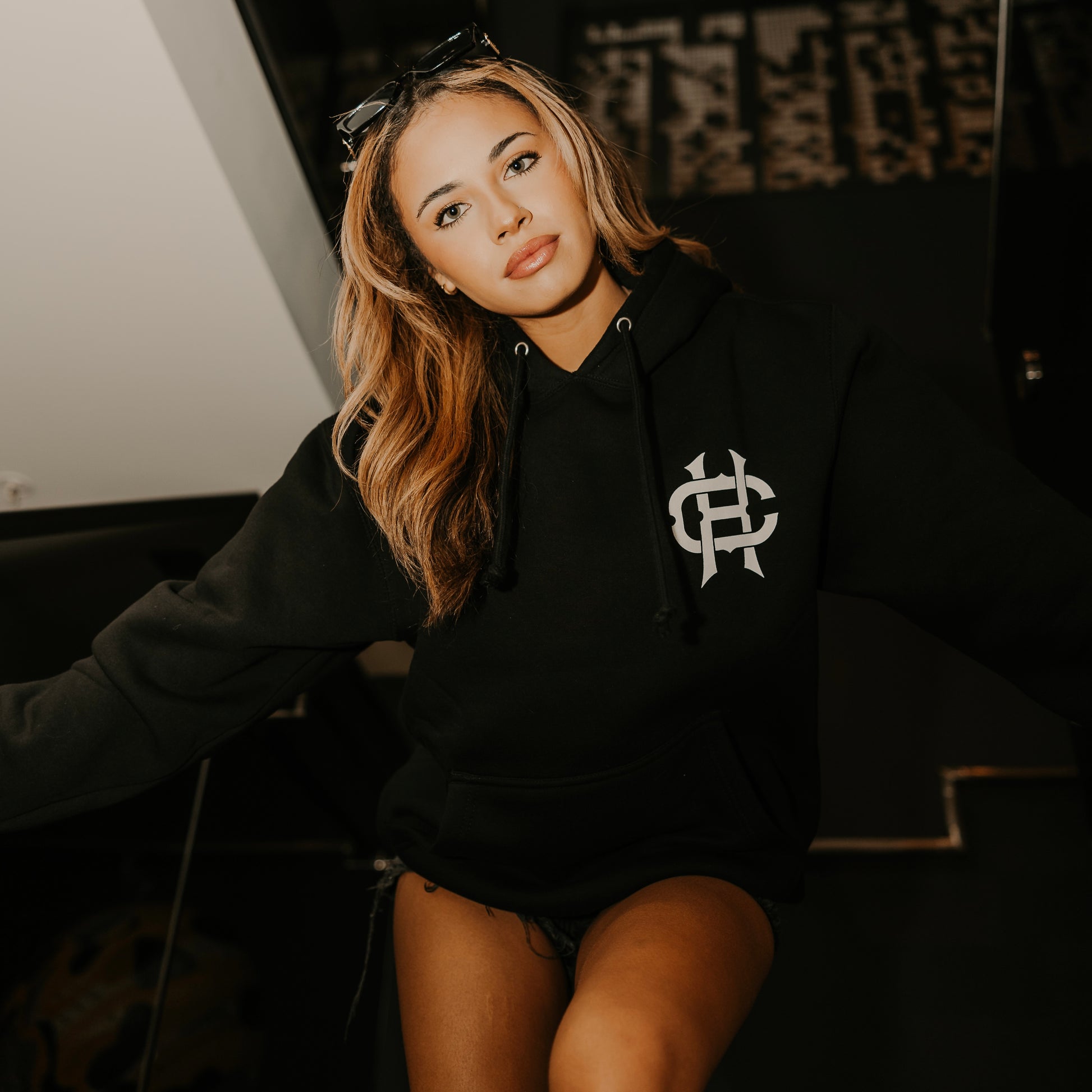 woman wearing true to the crew crossed heart black hoodie with chest logo tattoo inspired alternative streetwear hoodie indoor lifestyle