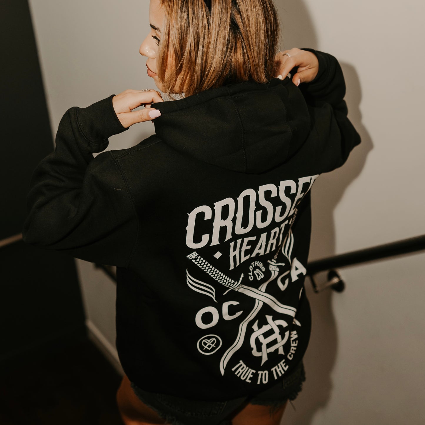 person wearing true to the crew crossed heart black hoodie with oc ca crossed swords graphic tattoo inspired alternative streetwear hoodie